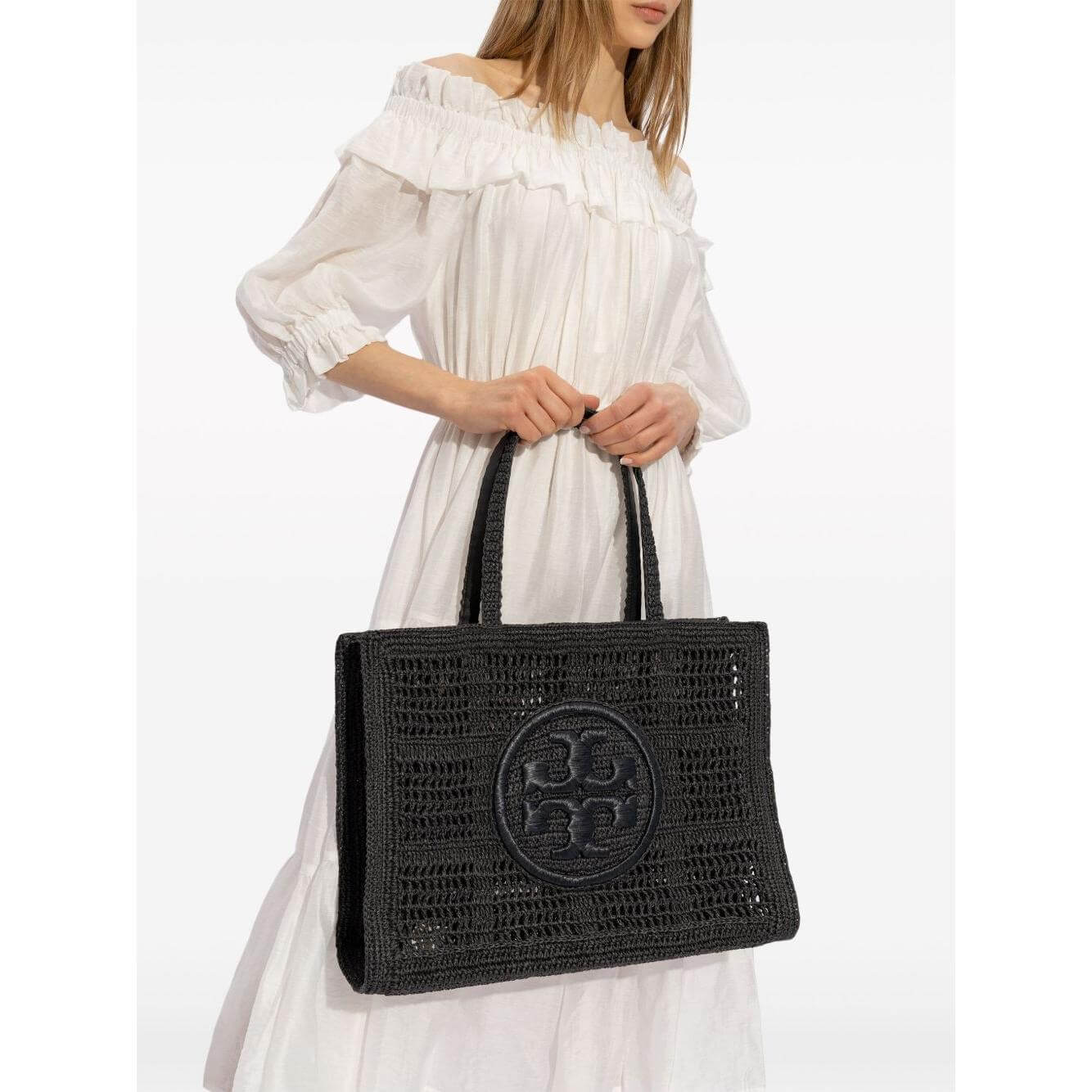 Woman holding Tory Burch Large Ella Crochet Tote Bag in black raffia with Double T motif and long handles.