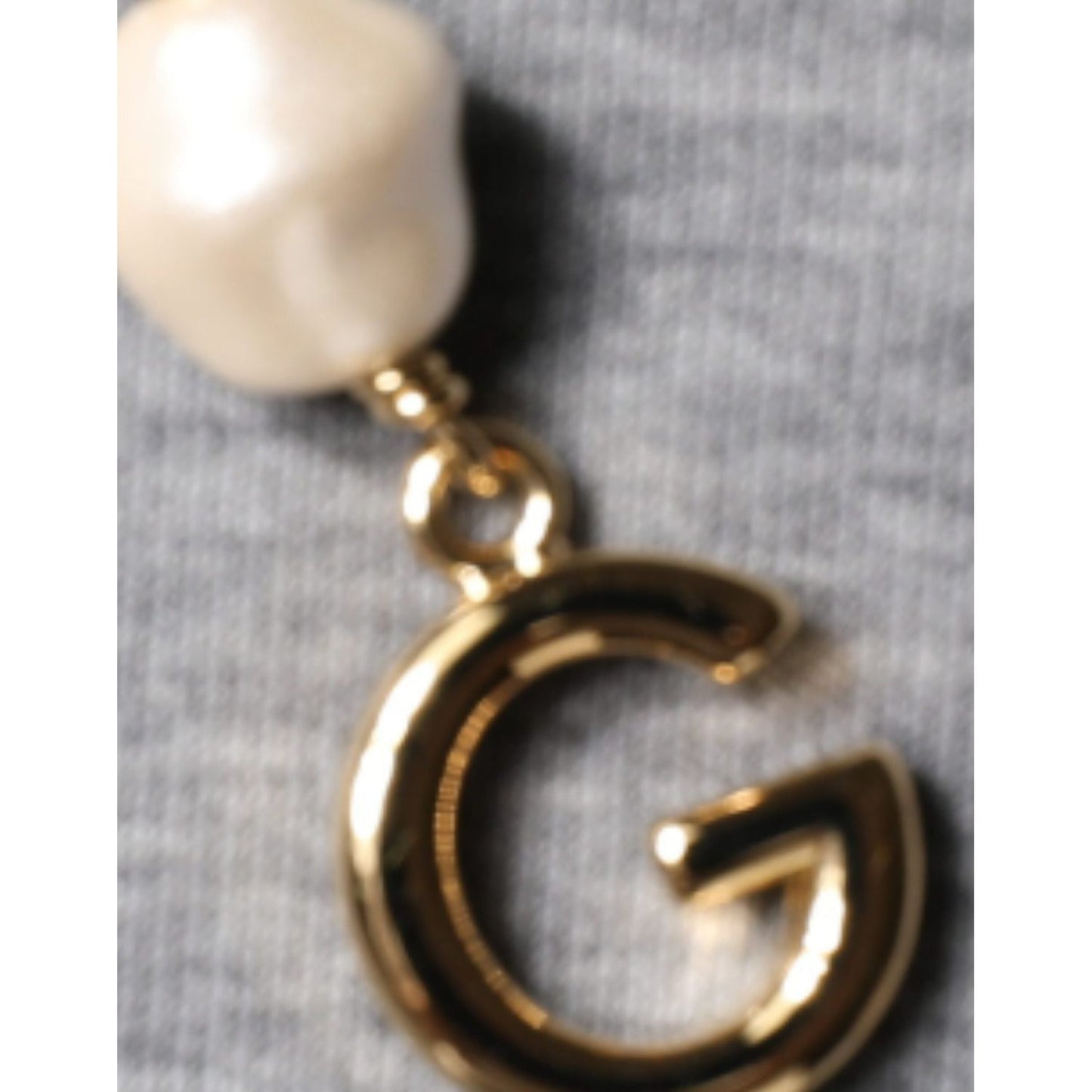 Dolce & Gabbana gold logo charm with pearl detail on gray cotton blend fabric.