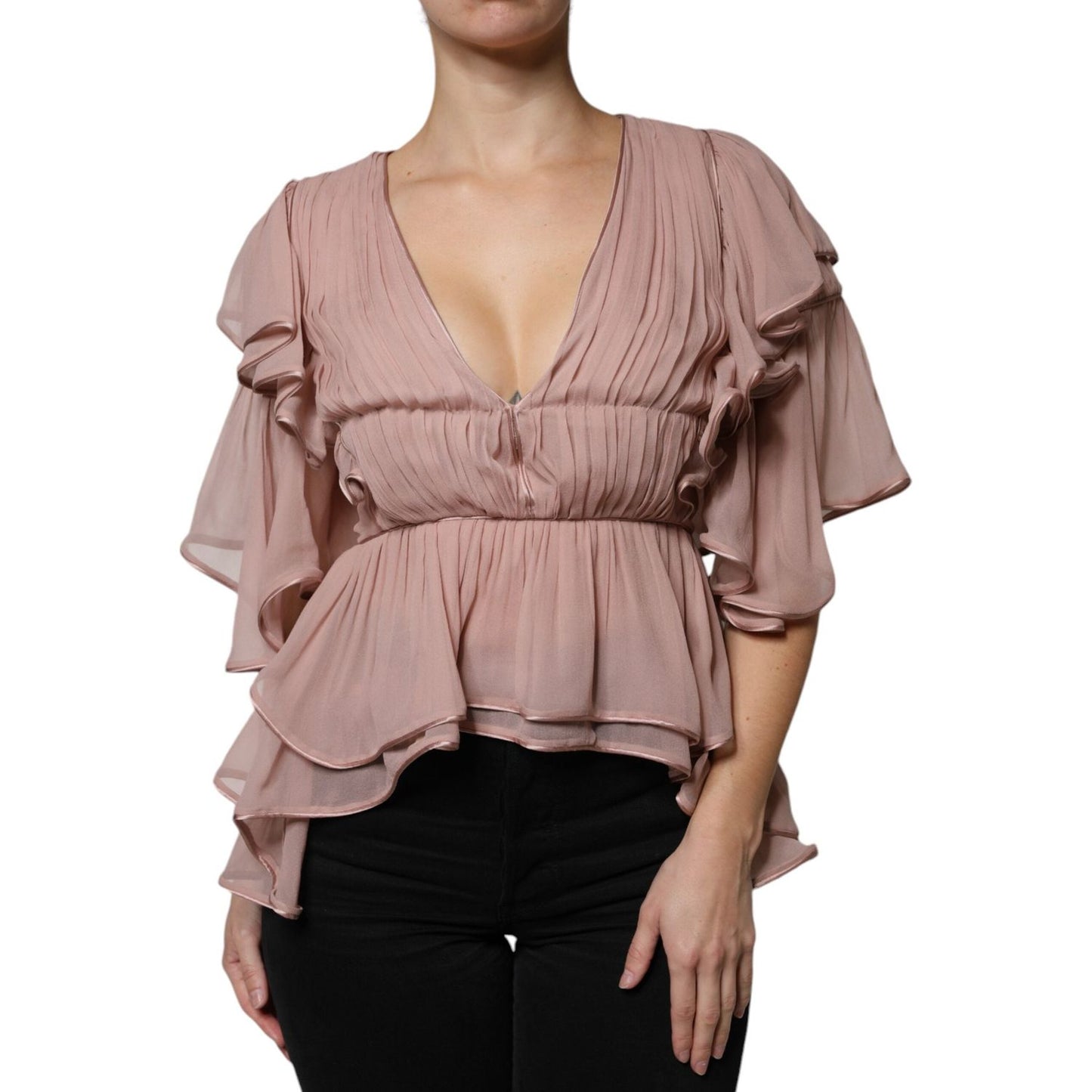Woman wearing a pink pleated V-neck top with ruffled short sleeves, paired with black pants. Fashionable and elegant outfit.