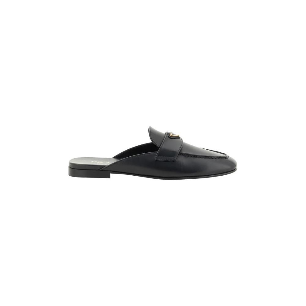 Prada leather mules with round toe and iconic triangular plaque, flat sole and contrasting logo insole, side view.