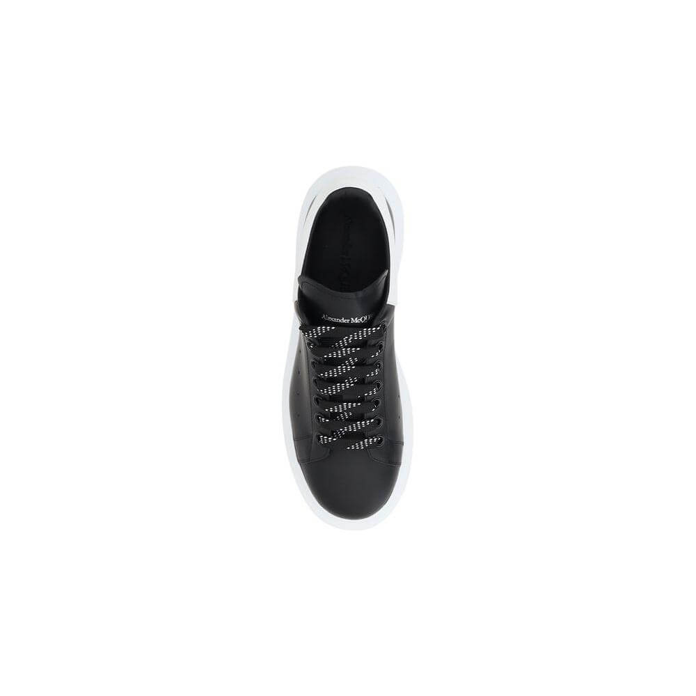 Top view of Alexander McQueen black leather sneakers with lace-up closure and logoed front tab on white background.