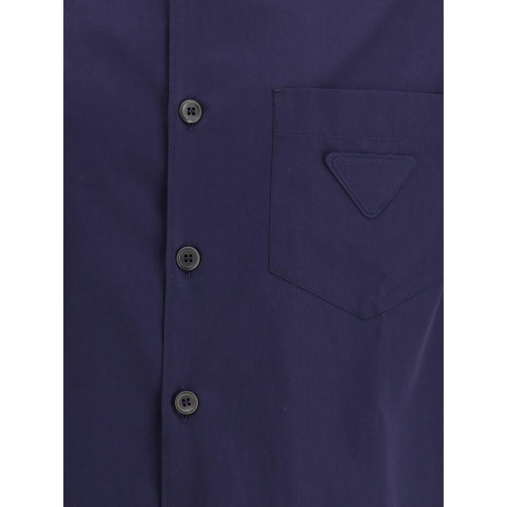 Prada short-sleeved navy cotton shirt with buttons, classic collar, and front pocket featuring iconic triangular patch, ideal for summer fashion.