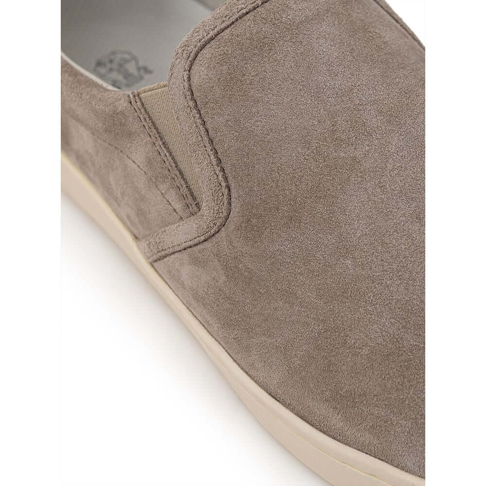Close-up of Brunello Cucinelli gray suede slip-on sneaker with contrasting white sole and black back detail, featuring gold 'Solomei' print.