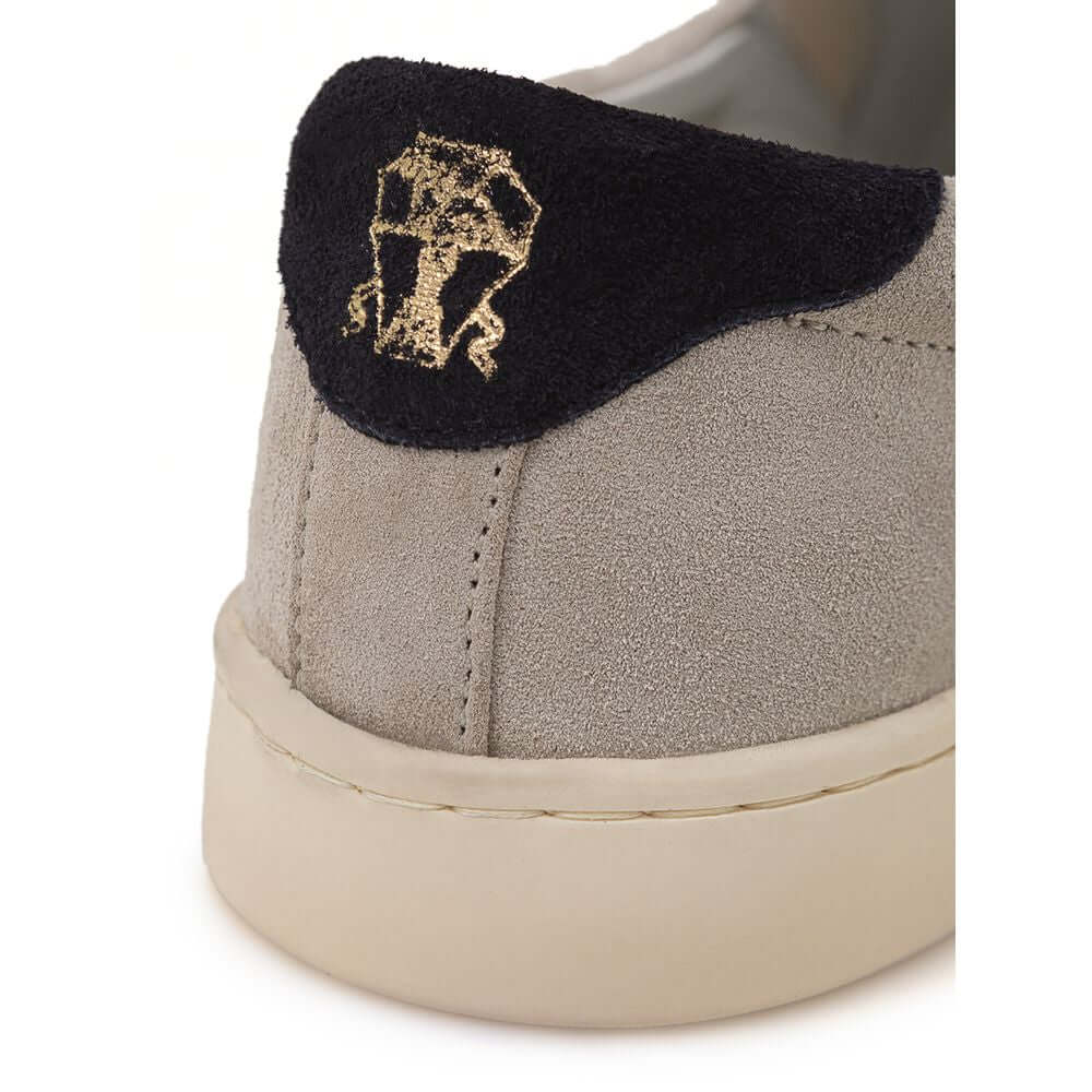 Close-up of Brunello Cucinelli gray leather sneaker with black suede back and gold 'Solomei' print, featuring white rubber sole.