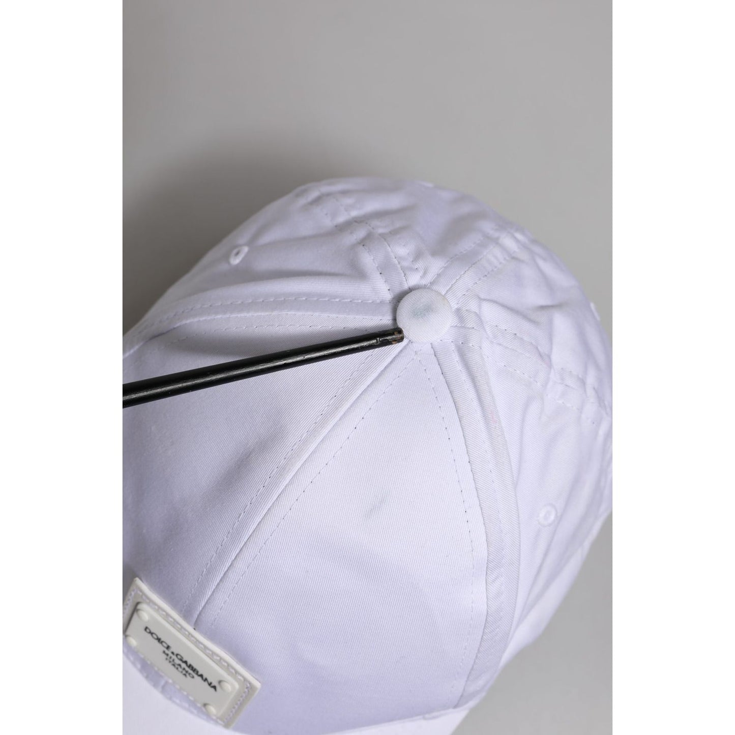 Top view of Dolce & Gabbana white baseball cap with logo plaque, showing minor stains on panels, made in Italy, cotton-elastane blend.