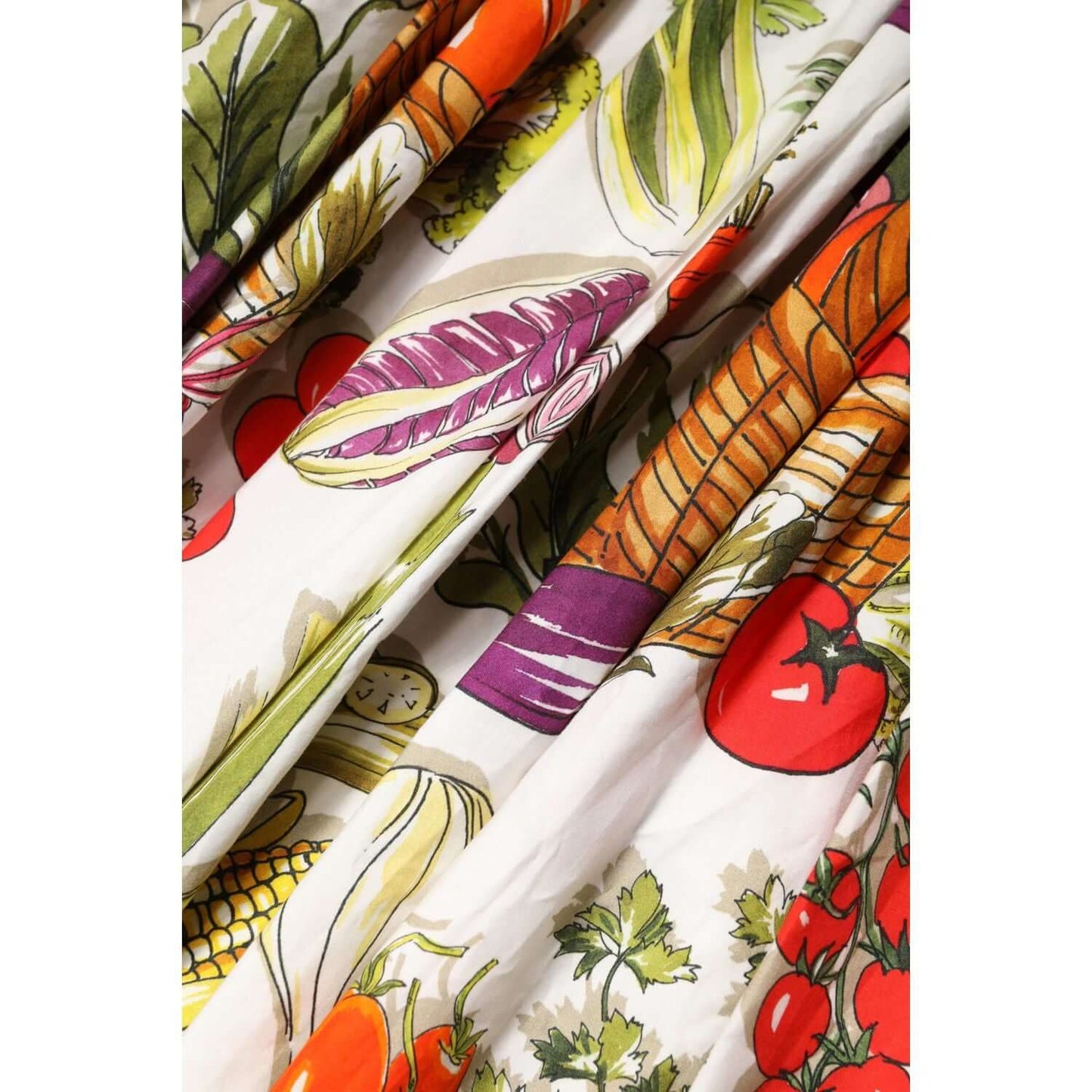Close-up of Dolce & Gabbana white dress with colorful vegetable print, featuring tomatoes, carrots, and lettuce. A-line, cotton fabric.