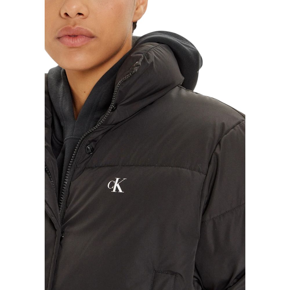 Woman wearing Calvin Klein Jeans Black Polyester Jacket, featuring cropped puffer style for warmth and fashion with CK logo.