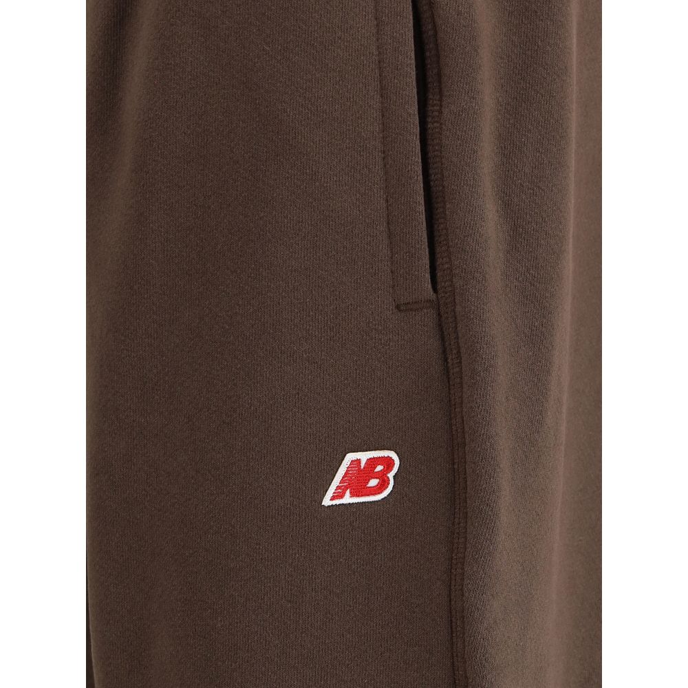 Close-up of New Balance Brown Cotton Joggers (Workout Pants) featuring logo patch and pocket detail with elasticated hem.