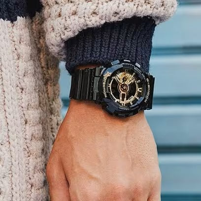 Person wearing CASIO G-SHOCK Mod. GS-BASIC - BLACK ADN GOLD SERIES wristwatch with resin strap and multifunction dial.