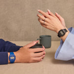 Two hands wearing CASIO VINTAGE Mod. F-91 BIO RESIN STRAP - BLUE and black watches over a table with coffee cups.