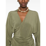 Model wearing olive green Cortana Cortana Serp Silk Jumpsuit with V-neck and tied waist, showcasing long sleeves and draped design.