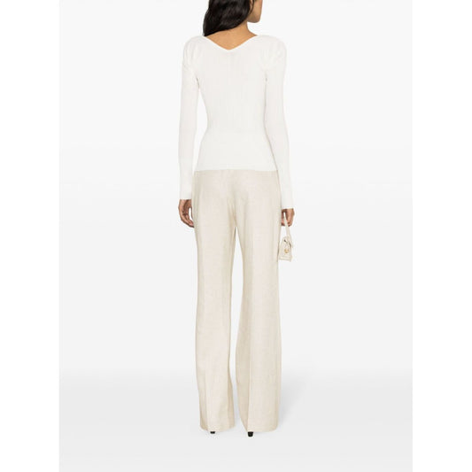 Back view of model wearing JACQUEMUS Top White with long sleeves and scallop edge, paired with neutral pants, showcasing V-neck and ribbed design.