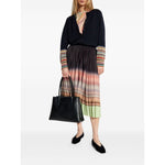 Woman wearing a stylish pleated multicolor dress with a black long-sleeve top, holding a black handbag and wearing black flats.