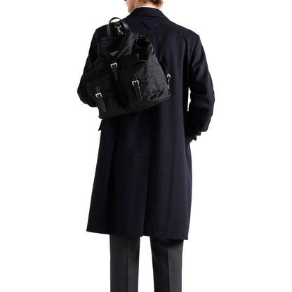 Man wearing Prada Blue Wool Coat with black backpack, showing back triangle logo detail, long sleeves, and straight hemline, made in Italy.