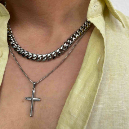 Close-up of a person wearing silver chains and a cross pendant with a yellow shirt, showcasing layered jewelry style.